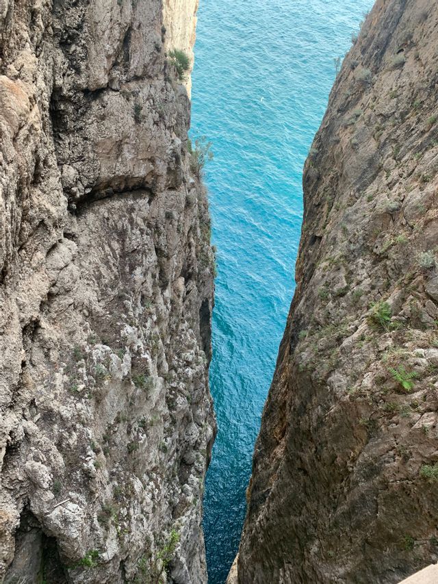 Una vista che si affaccia attraverso una stretta fessura tra due scogliere a picco verso l'acqua turchese del mare sottostante.