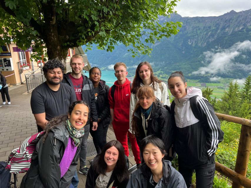 Un groupe WeRoad pose pour une photo à un point de vue, avec un lac turquoise et des montagnes vertes visibles en arrière-plan.