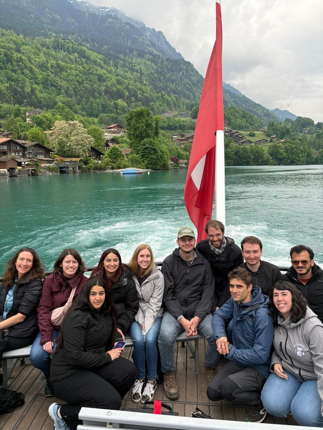 Un voyage de groupe WeRoad pose pour une photo sur un bateau sur un lac turquoise, avec un drapeau suisse et une montagne boisée en arrière-plan.