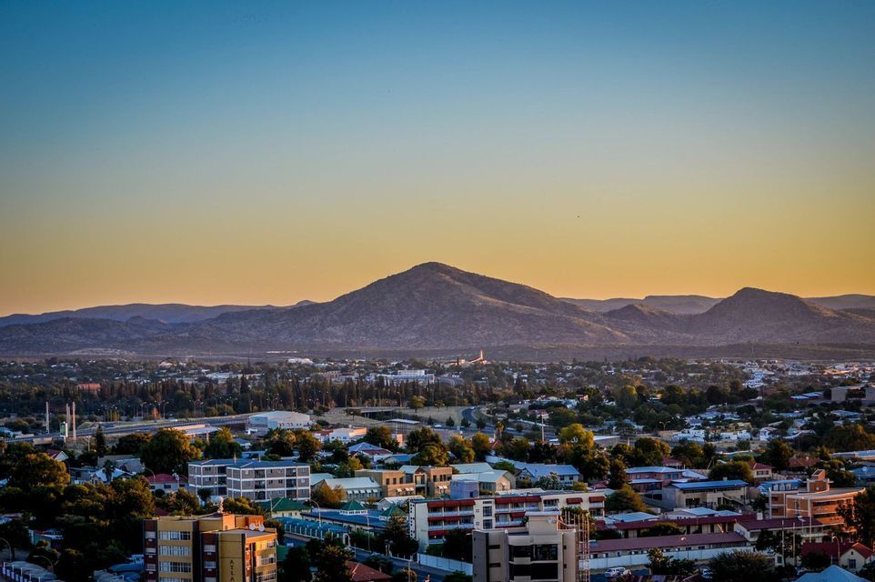 Eine Luftaufnahme einer Stadt mit Gebäuden und Bäumen, eingebettet am Fuße von Bergen unter einem goldenen Sonnenuntergangshimmel.