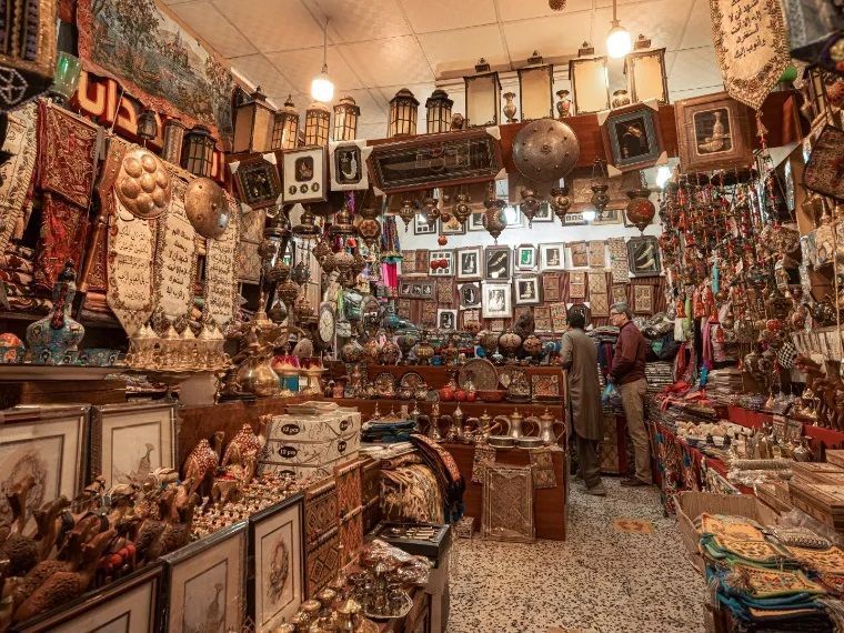 Intérieur d'une brocante encombrée, remplie de lanternes, d'objets d'art et de cadres, avec deux hommes qui examinent les articles.