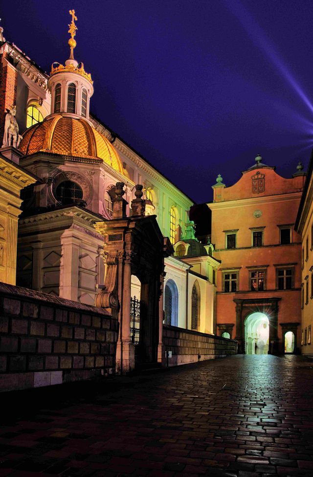 Una histórica calle empedrada de noche, con un edificio ornamentado que presenta una gran cúpula dorada iluminada contra un cielo oscuro.