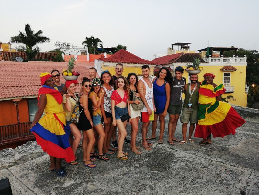 Un groupe WeRoad pose pour une photo sur un toit, avec deux femmes portant des robes traditionnelles colorées et équilibrant des fruits sur leur tête.