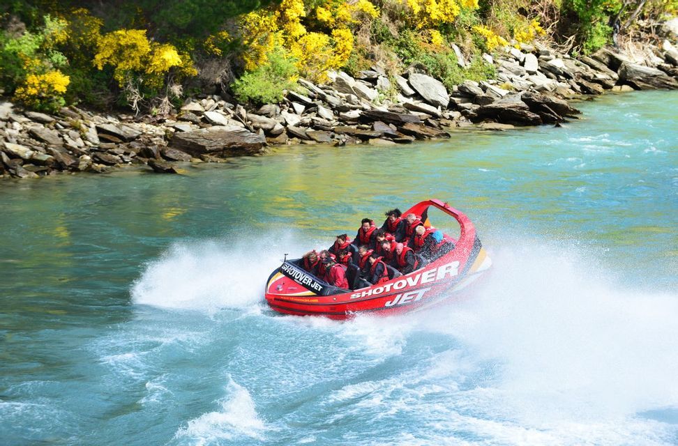 A WeRoad group trip of people in a red jet boat speeding through turquoise river water, creating a large white wake.