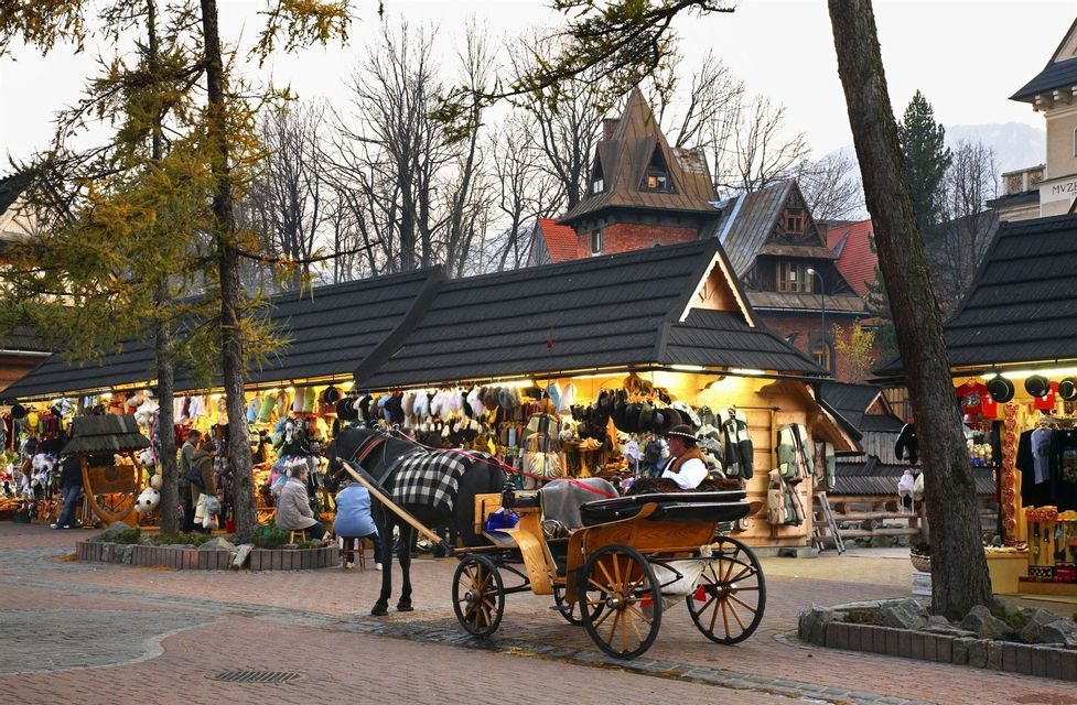 A horse-drawn carriage with a driver waits on a cobblestone street in front of illuminated market stalls with wooden buildings behind.