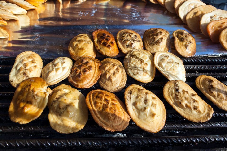 Grilled smoked cheeses with decorative patterns arranged on a black metal grill at a food stall.