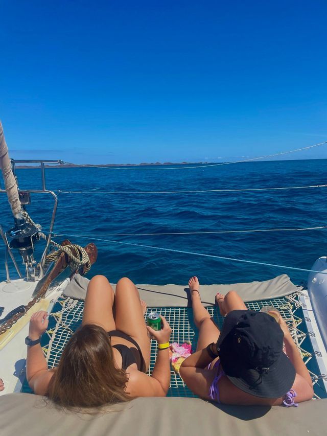 Dos mujeres de un viaje en grupo de WeRoad toman el sol en la red de un catamarán mientras navegan en el mar azul.