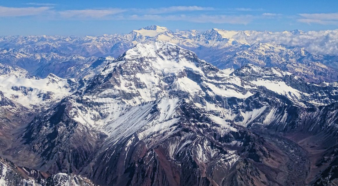 An aerial view of a vast mountain range with snow-covered peaks under a clear blue sky.