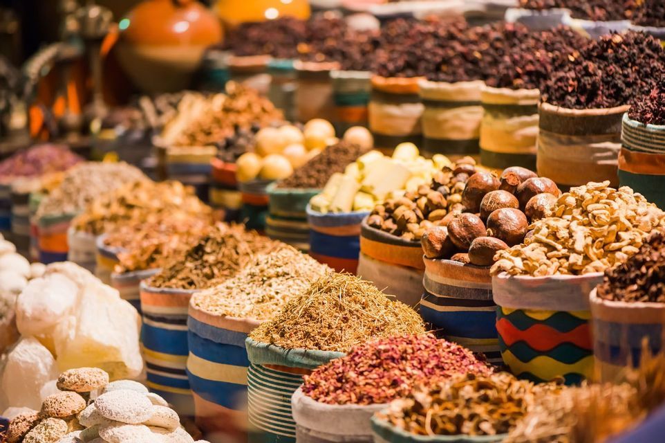 Eine Nahaufnahme verschiedener Gewürze, Kräuter und Nüsse, die in bunten, gestreiften Säcken an einem Marktstand präsentiert werden.