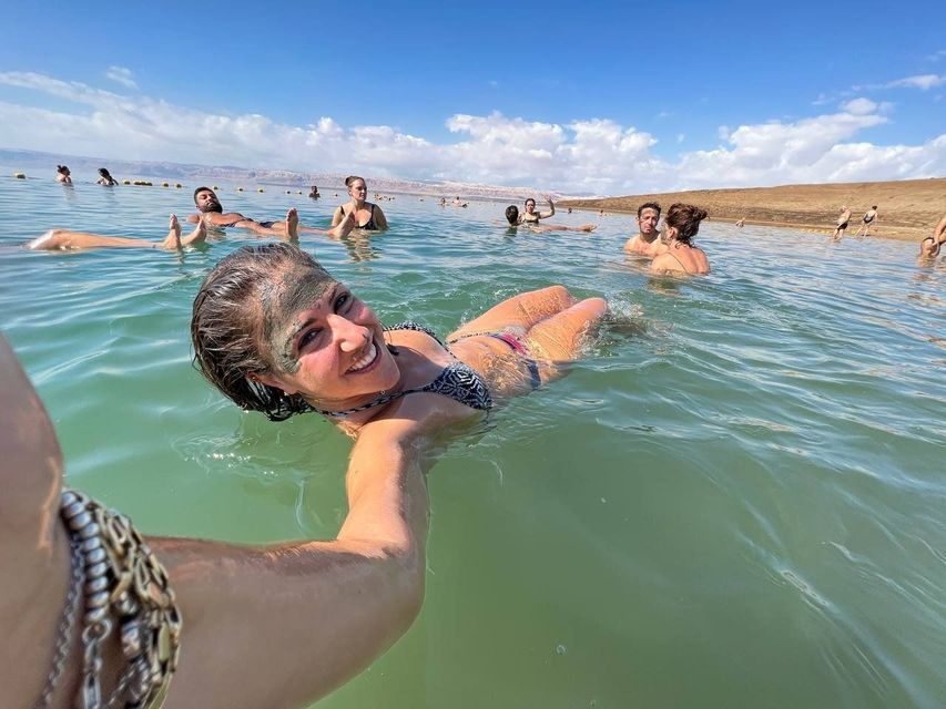 Una mujer sonriente con barro en la cara se toma una selfie mientras flota en el agua en un viaje en grupo de WeRoad.