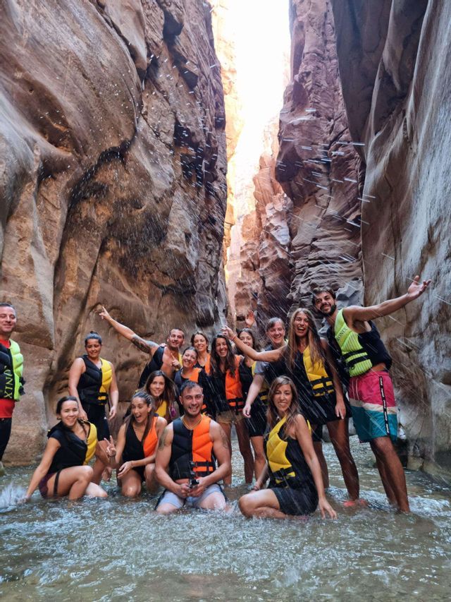 Eine WeRoad-Gruppe in Schwimmwesten posiert für ein Foto, während sie in einem engen Canyon im Wasser planscht.