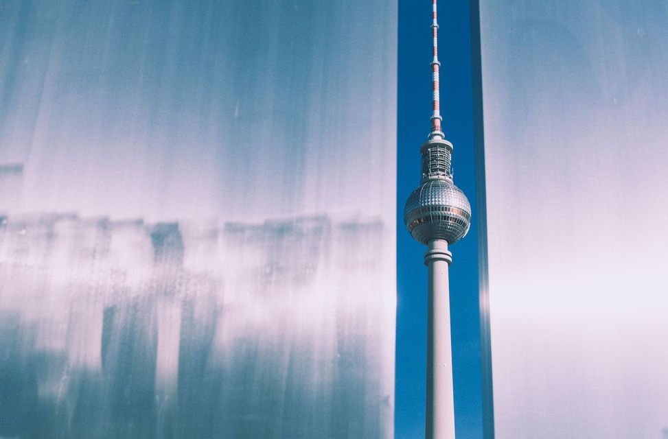La Torre de Televisión de Berlín está enmarcada entre dos estructuras grises abstractas y borrosas contra un cielo azul brillante.