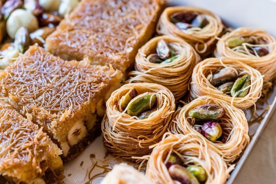 Un primer plano de variados pasteles de Oriente Medio, que incluyen nidos de masa desmenuzada rellenos de pistachos y baklava cuadrado con avellanas.
