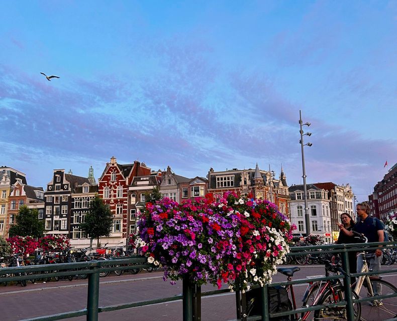 Bunte Blumen in einem Hängekübel auf einer Brücke mit Blick auf eine Straße mit traditionellen Giebelhäusern bei Dämmerung.