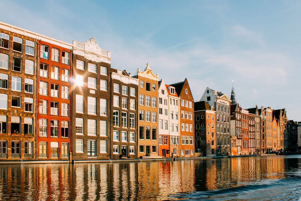 La luz del sol crea un destello brillante en una hilera de edificios coloridos a lo largo de un canal, sus fachadas reflejándose en el agua.