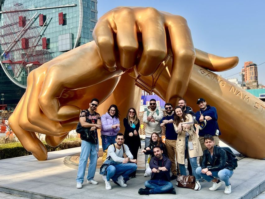 Un viaggio di gruppo WeRoad in posa davanti a una scultura gigante dorata di mani incrociate in una piazza urbana.