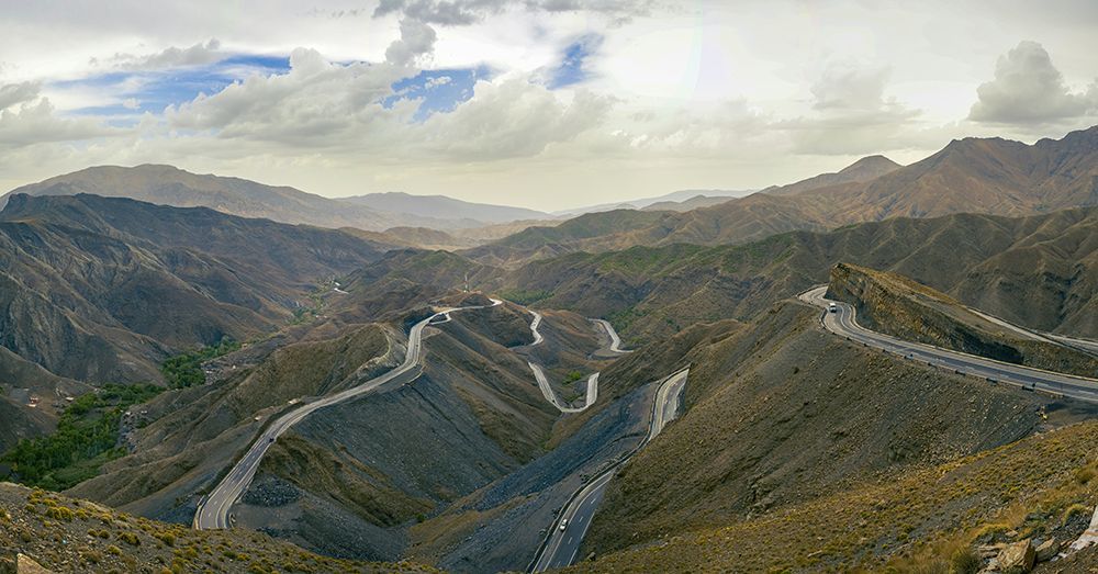 Una vista panoramica di una strada tortuosa che attraversa una vasta catena montuosa rocciosa sotto un cielo nuvoloso.