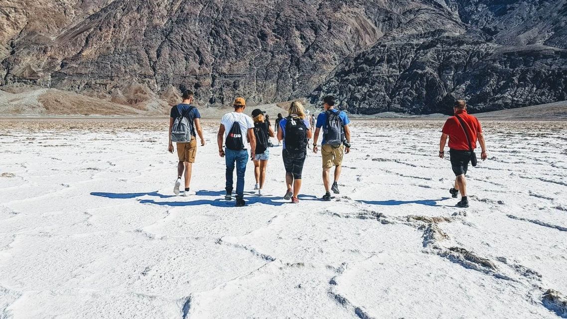 Un viaggio di gruppo WeRoad attraversa una vasta distesa di sale bianca con montagne rocciose sullo sfondo.