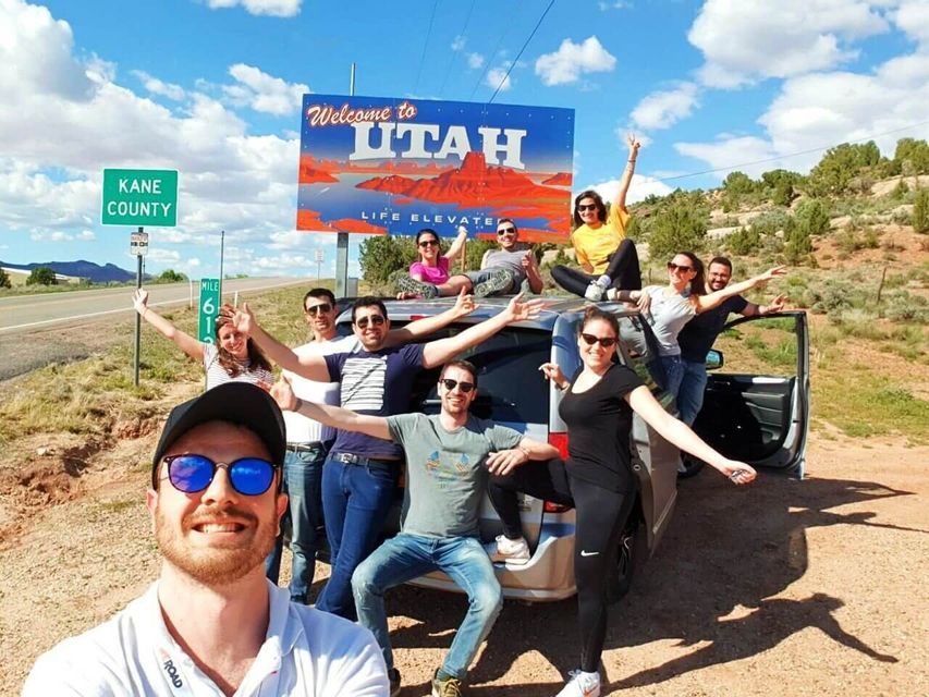 Eine WeRoad-Gruppe macht ein lächelndes Selfie mit ihrem Auto vor einem 'Welcome to Utah'-Schild.