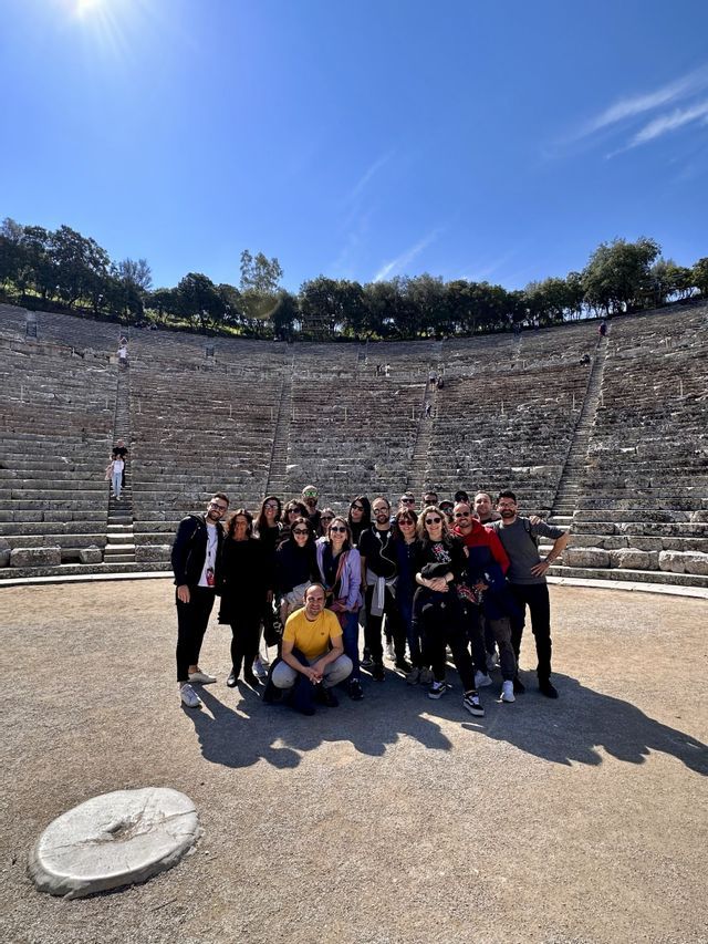 Un gruppo WeRoad posa per una foto al centro di un grande anfiteatro in pietra sotto un cielo azzurro.