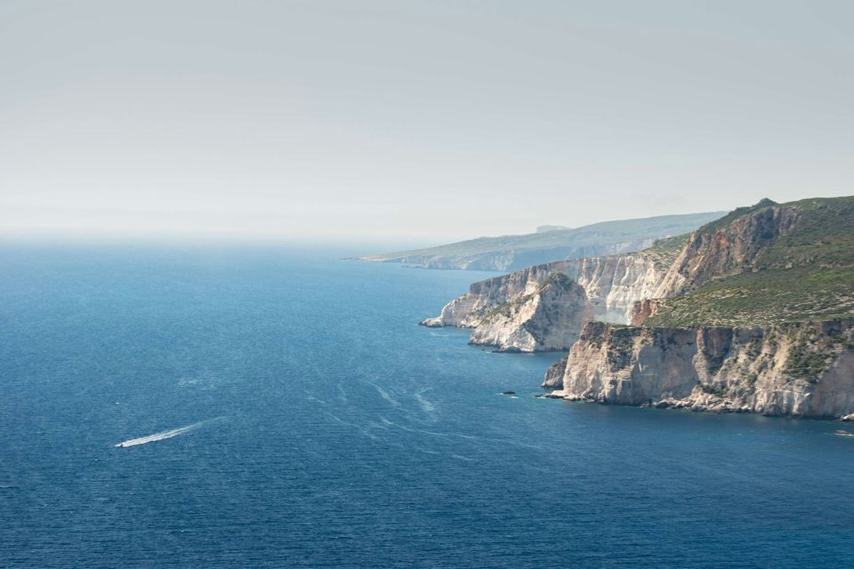 Un motoscafo crea una scia bianca sul mare blu intenso mentre passa una costa scenografica con scogliere bianche.