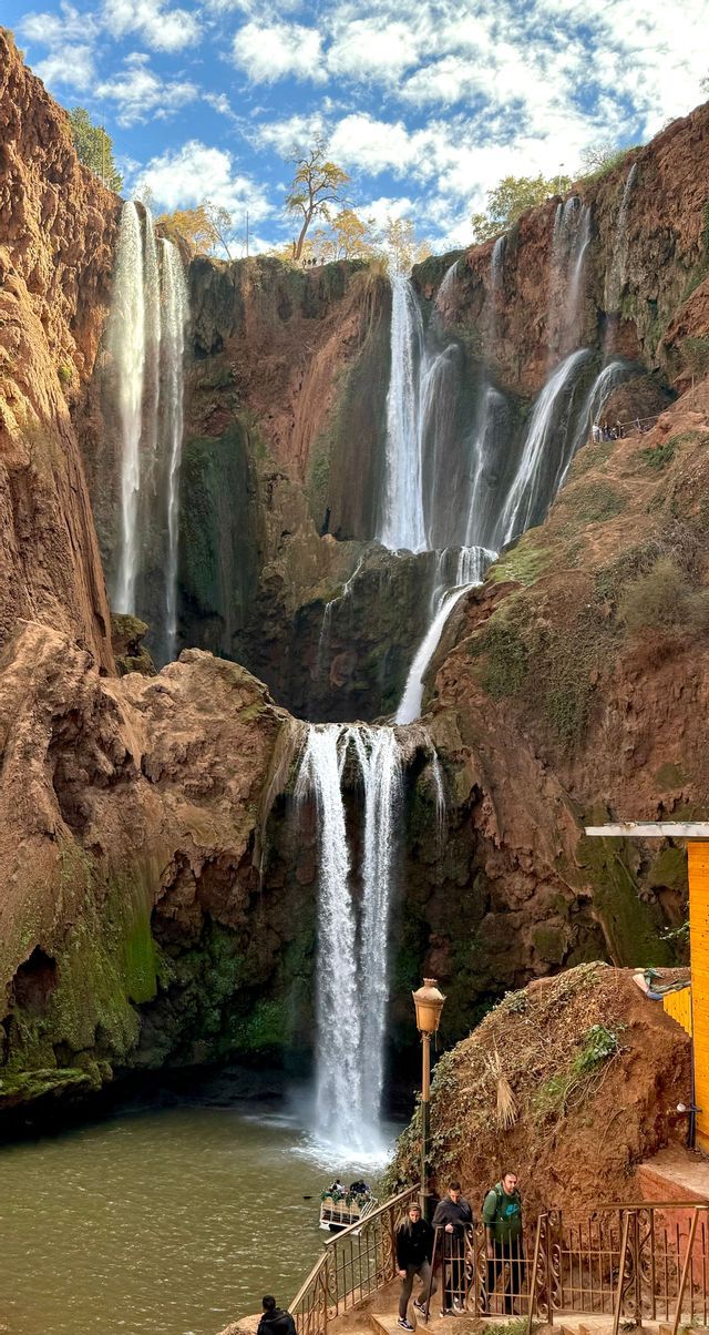 Un viaggio di gruppo WeRoad ammira un'ampia cascata a più livelli che scende da scogliere di roccia rossa in una piscina naturale.