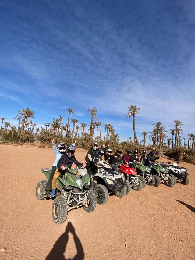 Un gruppo WeRoad in viaggio posa con i caschi sui quad in un palmeto sabbioso sotto un cielo azzurro.