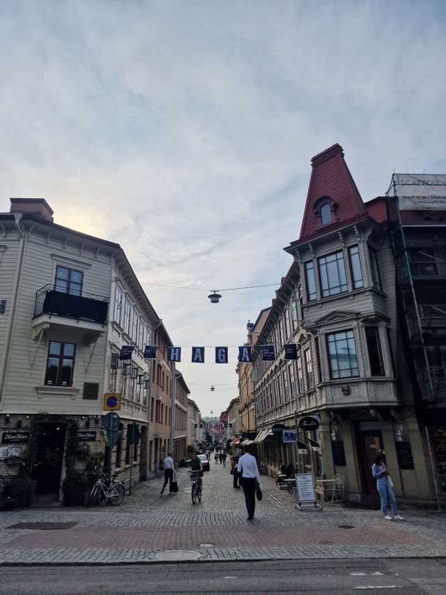 Menschen gehen und radeln auf einer Kopfsteinpflasterstraße, die von traditionellen, mehrstöckigen Gebäuden unter einem bewölkten Himmel gesäumt ist.