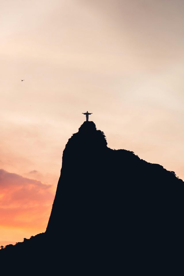 La estatua del Cristo Redentor recortada en una cima montañosa contra un atardecer de colores vivos.