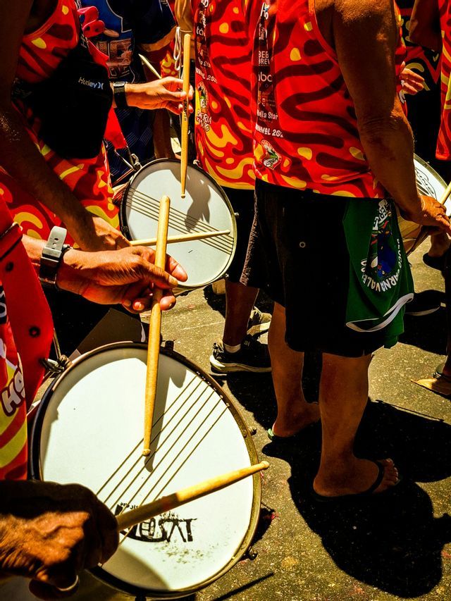 Primer plano de un viaje en grupo de WeRoad tocando tambores en camisas coloridas rojas y amarillas durante un festival callejero soleado.