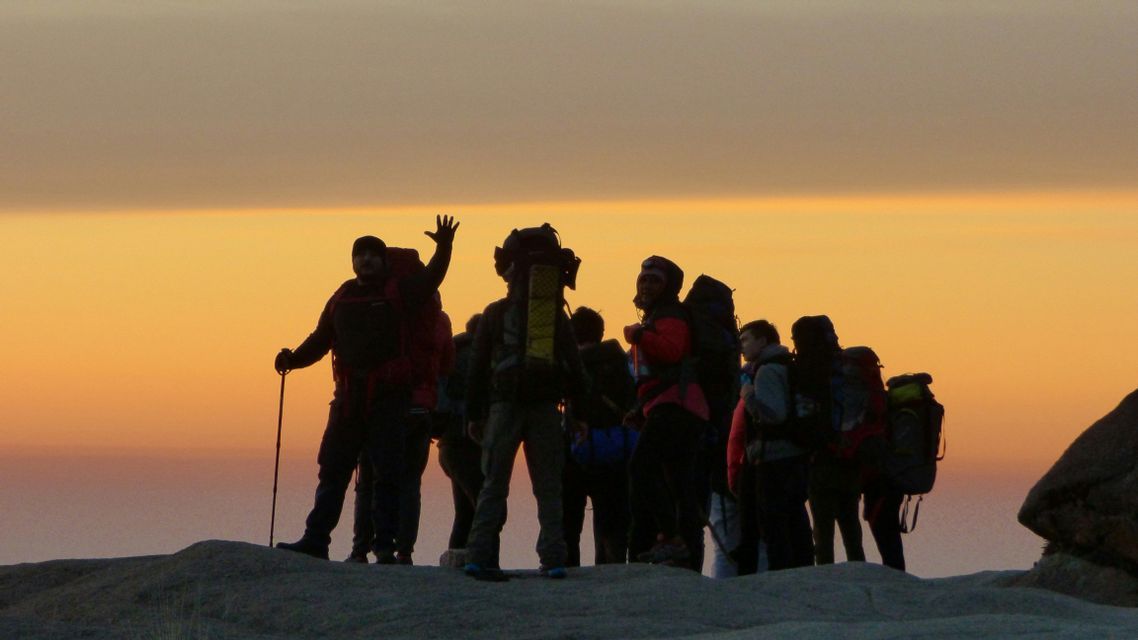 Un gruppo di escursionisti WeRoad con zaini è stagliato su una collina contro un cielo dorato al tramonto.