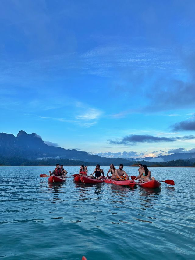 Eine WeRoad Gruppenreise beim Kajakfahren auf einem See in roten Booten, mit nebligen Bergen im Hintergrund unter blauem Himmel.