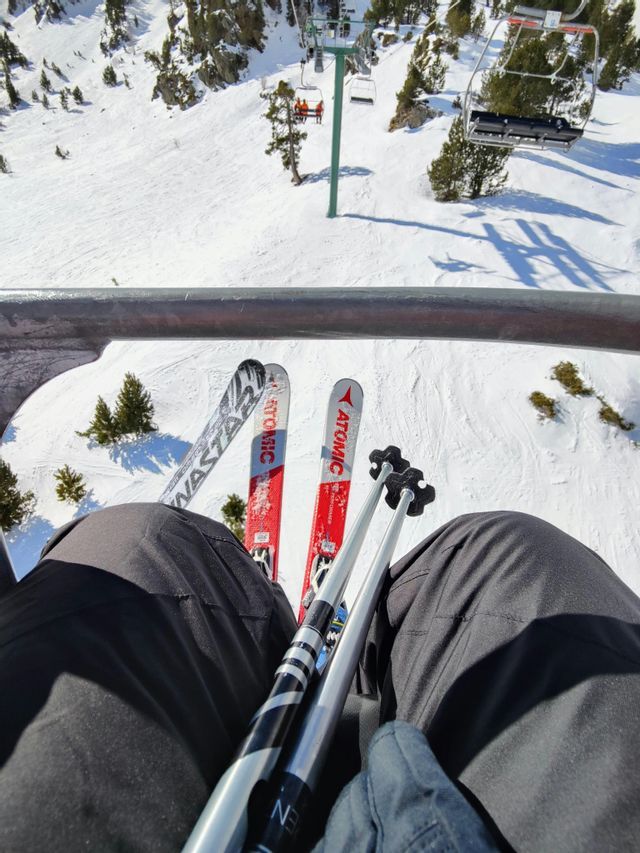 Una perspectiva en primera persona desde un telesilla, con esquís y bastones apoyados en el regazo, con vistas a una ladera de montaña cubierta de nieve.