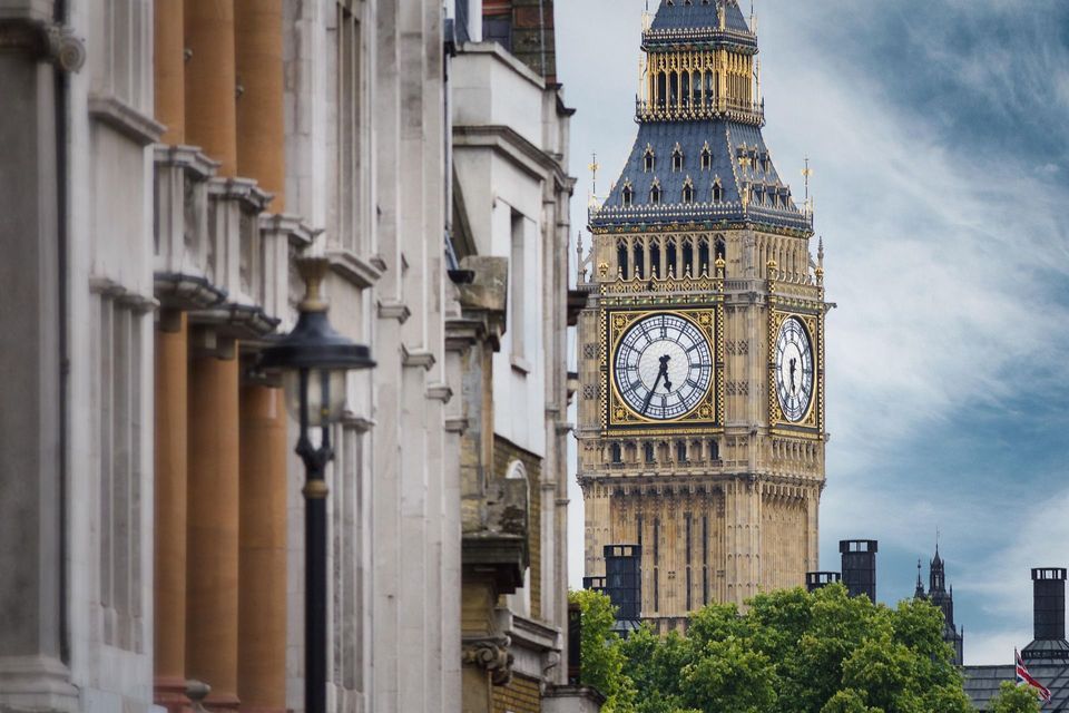 Una vista de la torre del reloj Big Ben enmarcada por edificios de la ciudad y copas de árboles bajo un cielo nublado.