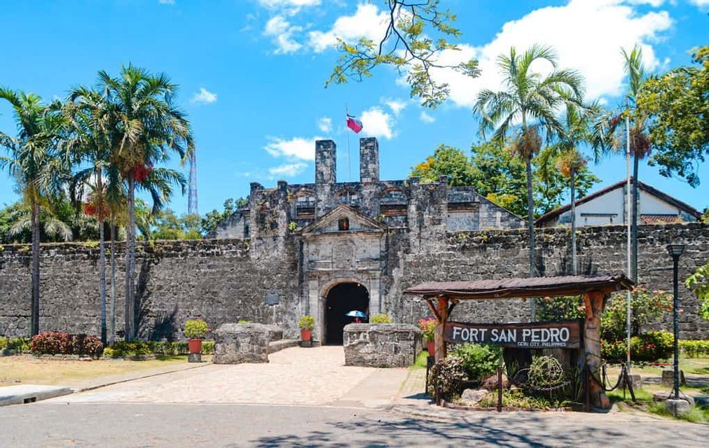L'ingresso al Forte San Pedro, un forte storico in pietra con un portale ad arco, affiancato da palme sotto un cielo azzurro.