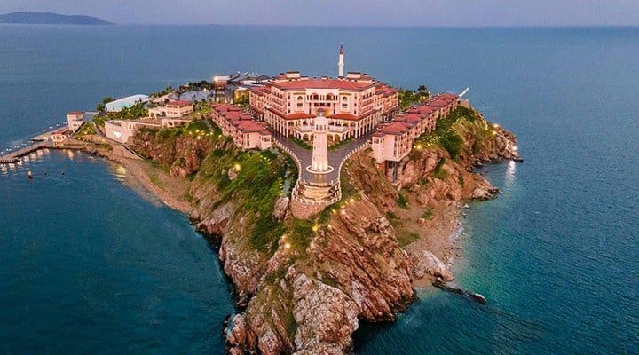 Vue aérienne d'un grand complexe hôtelier illuminé sur une péninsule rocheuse entourée par la mer au crépuscule.