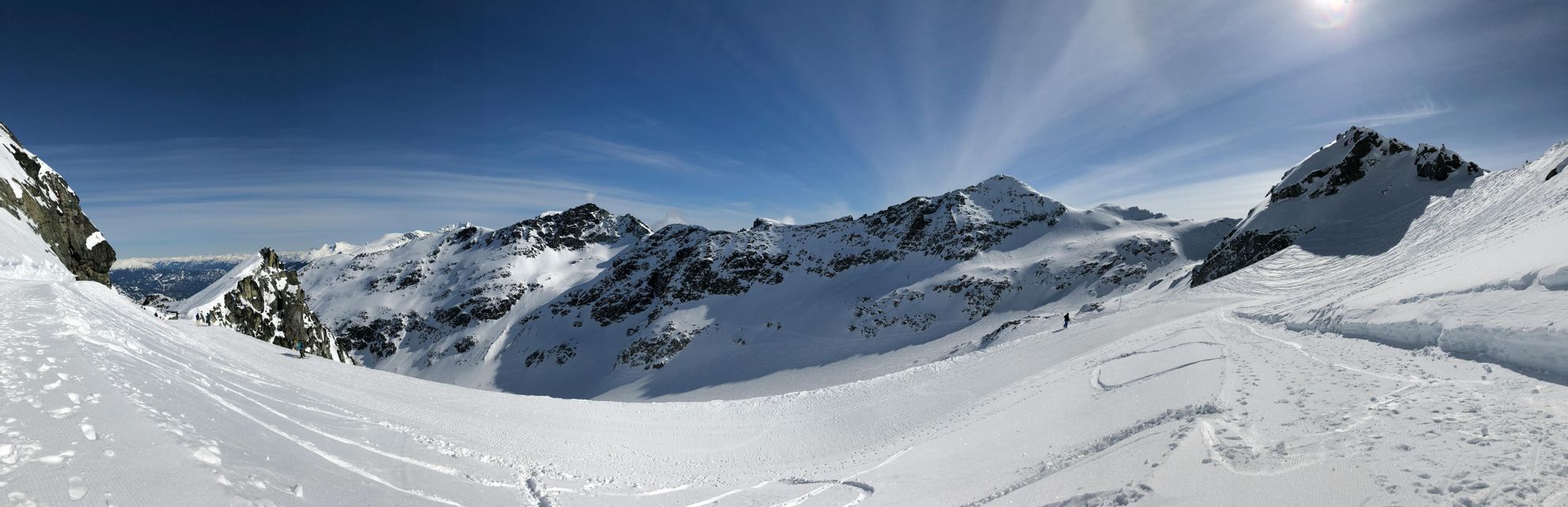 Un'ampia vista panoramica di una vasta catena montuosa innevata sotto un cielo azzurro limpido, con tracce di sci visibili sulle piste.