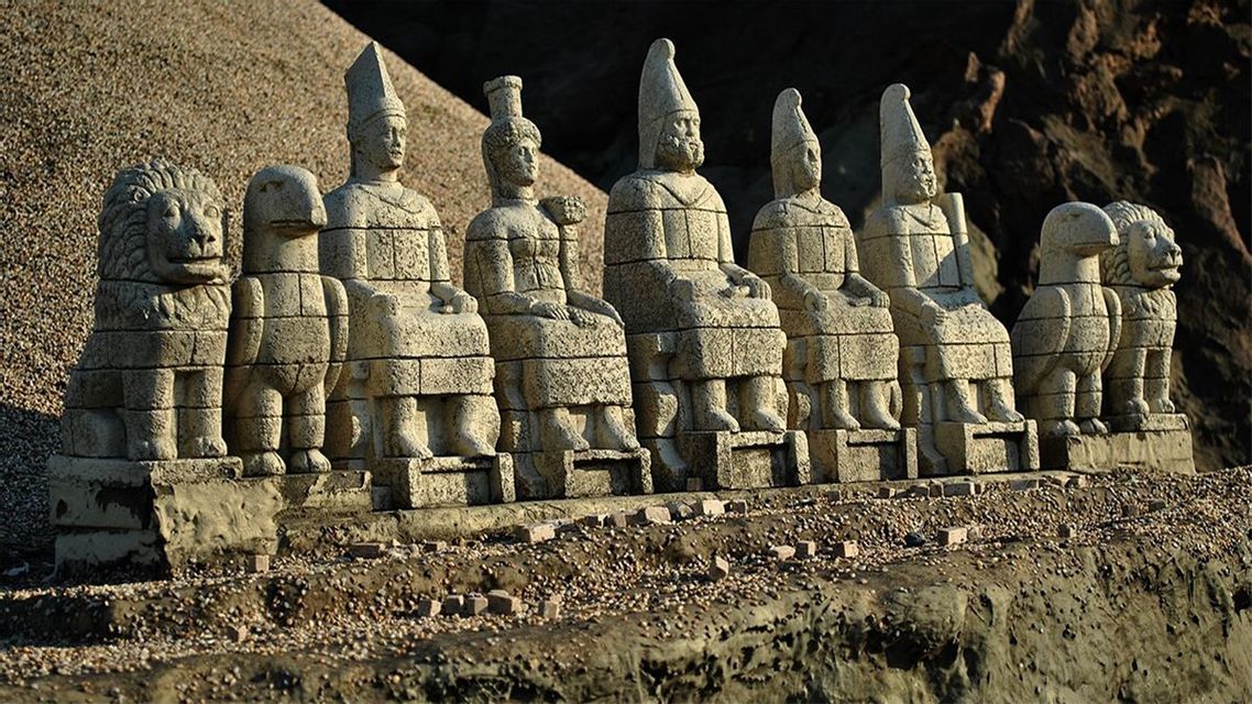 Une rangée d'anciennes statues en pierre, représentant des figures assises, un lion et un aigle, sur une terrasse.