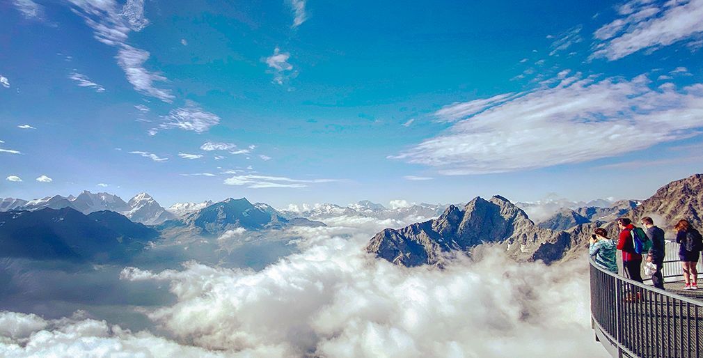 Un gruppo WeRoad si trova su una piattaforma panoramica, ammirando un mare di nuvole e una vasta catena montuosa.