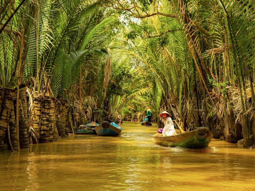 Un viaggio di gruppo WeRoad remando su piccole barche di legno lungo un fiume stretto, circondato da palme lussureggianti.