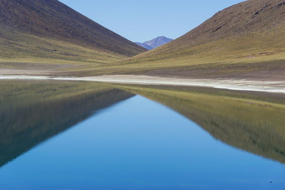 Due versanti montuosi in pendenza creano una valle e si riflettono perfettamente nell'acqua calma di un lago.