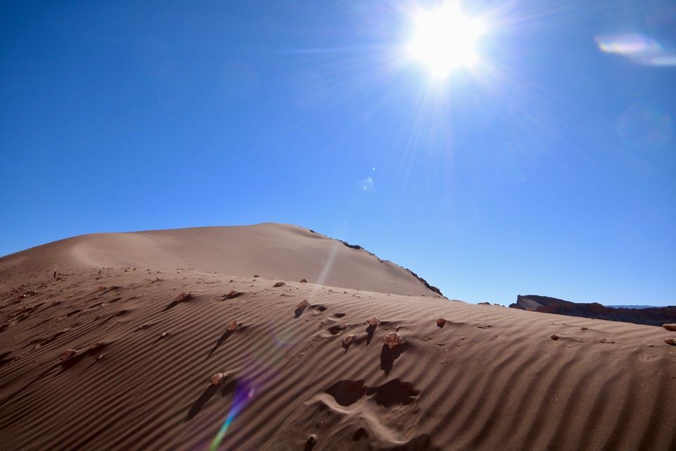 Una vasta duna di sabbia con increspature sotto un sole splendente e un cielo azzurro limpido.
