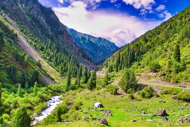 Une seule tente est dressée sur une prairie verdoyante au bord d&#39;une rivière dans une vaste vallée entourée de montagnes escarpées et couvertes d&#39;arbres.