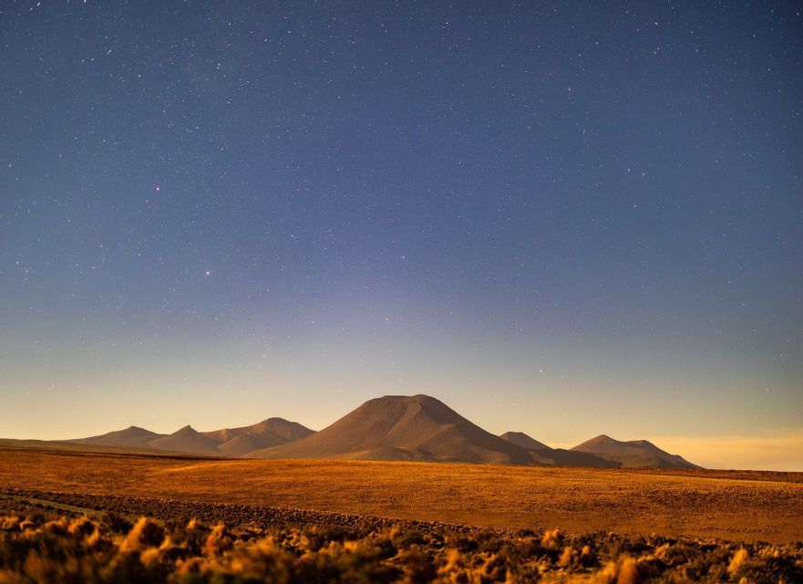 Un vasto paesaggio desertico dorato con montagne ondulate in lontananza sotto un cielo notturno limpido e stellato.