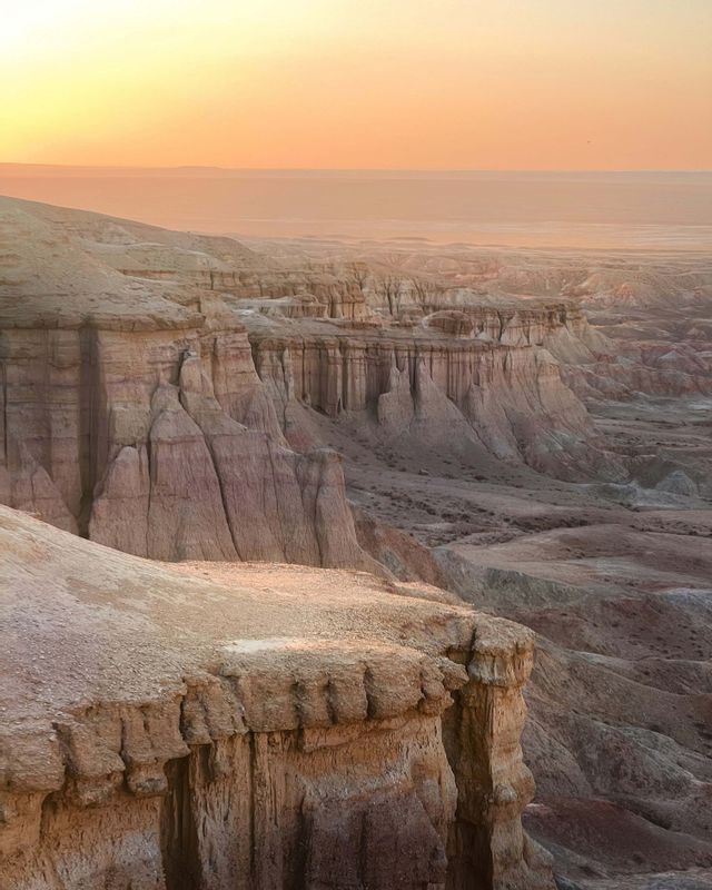 Eine weite Canyon-Landschaft mit geschichteten Felsformationen, die sich unter einem warmen, leuchtenden Himmel bei Sonnenaufgang in die Ferne erstrecken.