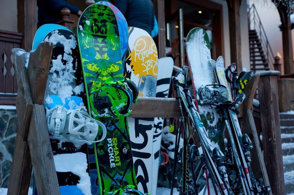 Des snowboards et des skis colorés, recouverts de neige, reposent sur un support en bois à l&#39;extérieur d&#39;un bâtiment.