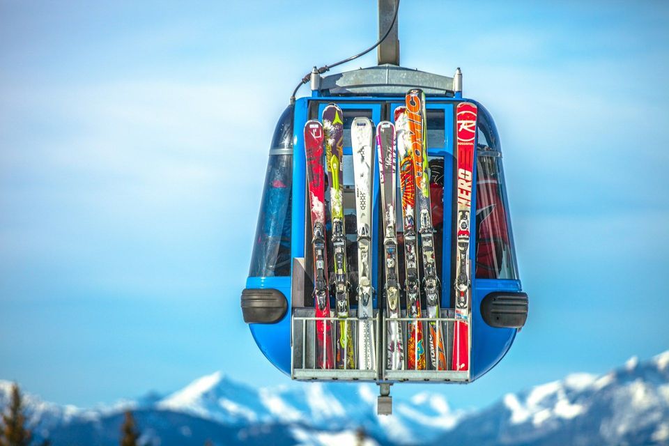 Une télécabine bleue transporte plusieurs paires de skis jusqu&#39;à un support extérieur, bien au-dessus des montagnes enneigées.