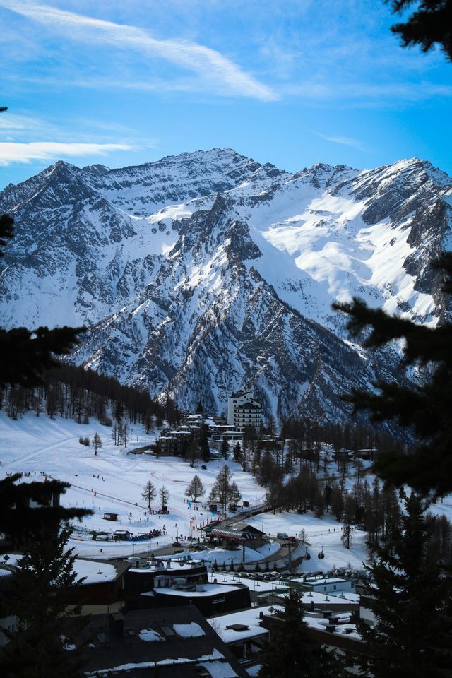 Vue aérienne d&#39;un village de ski dans une vallée enneigée, avec d&#39;imposantes montagnes enneigées en arrière-plan sous un ciel bleu.