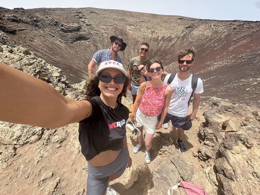 Un groupe WeRoad souriant prend un selfie sur le bord rocheux d'un grand cratère volcanique