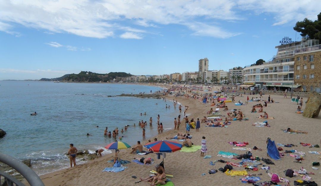 Un'ampia veduta di una spiaggia sabbiosa affollata con molte persone che nuotano nel mare e prendono il sole sulla sabbia vicino a una città costiera.